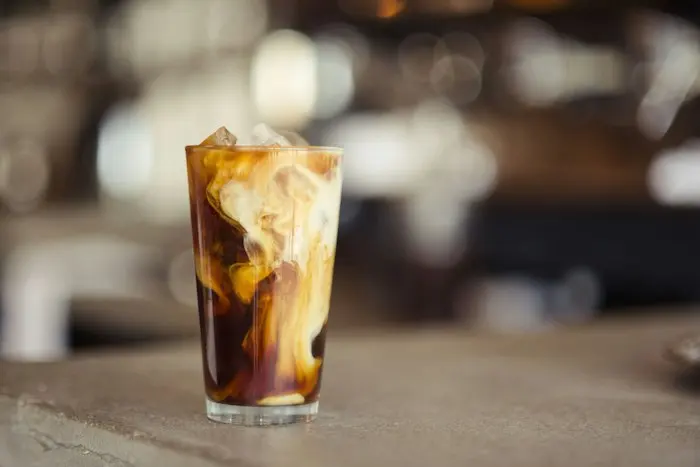 A glass of iced coffee with cream swirling through it