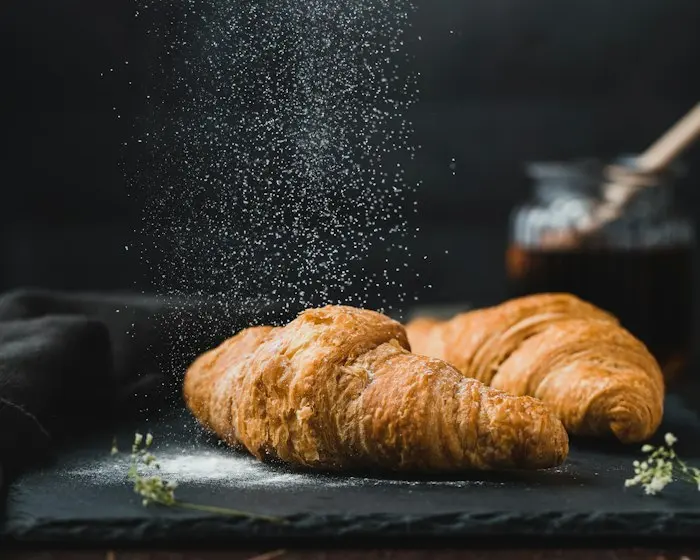 Golden croissants dusted with flour on a dark board